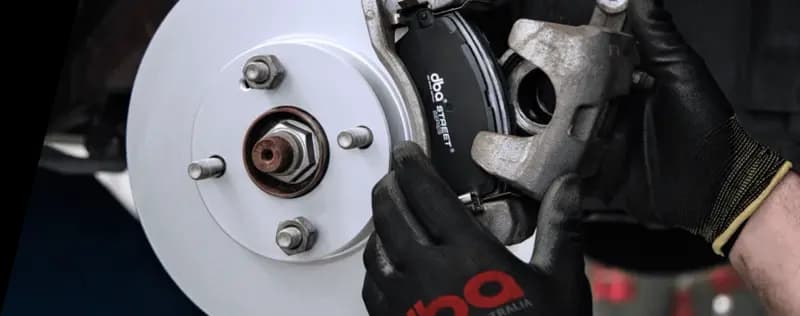 Mechanic in DBA-branded gloves installing brake rotor and caliper on vehicle wheel hub