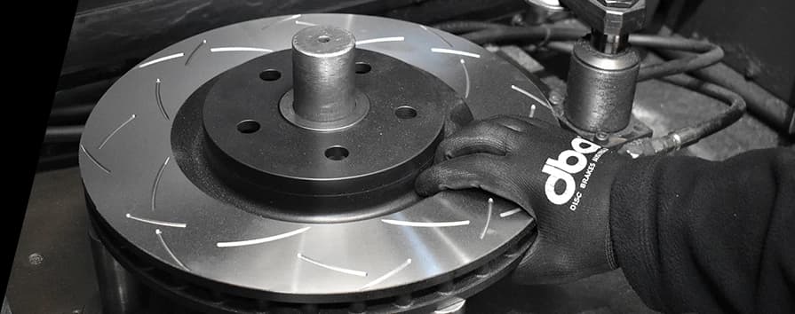 Close-up of technician wearing DBA gloves installing slotted performance brake rotor on vehicle hub during brake service