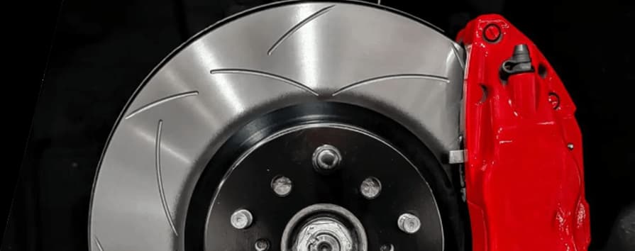 Close-up of DBA slotted performance brake rotor installed with bright red caliper on vehicle hub against black background