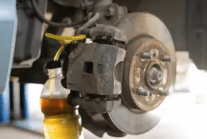 Brake fluid and air bubbles being expelled through bleeder valve into collection container during proper brake bleeding sequence Brake caliper with yellow collection tube attached to bleeder valve showing amber brake fluid flowing into clear container during bleeding