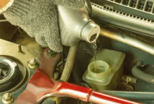 Replenishing brake fluid in master cylinder reservoir to prevent air introduction during the brake system bleeding process Mechanic's gloved hand pouring fresh brake fluid into master cylinder reservoir during brake bleeding procedure to maintain proper fluid level